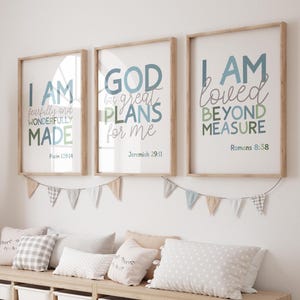 May include: Three framed wall art prints with light wood frames featuring blue and green typography. The prints display the text: I AM fearfully and wonderfully MADE Psalm 139:14, GOD has great PLANS for me Jeremiah 29:11, and I AM loved BEYOND MEASURE Romans 8:38.