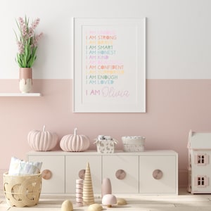 Puede incluir: Una impresi&oacute;n enmarcada blanca con un fondo rosa y texto de color arco&iacute;ris que dice "Soy &uacute;nica, soy fuerte, soy valiente, soy inteligente, soy honesta, soy amable, soy hermosa, soy segura de m&iacute; misma, soy apoyada, soy suficiente, soy amada, soy Olivia".