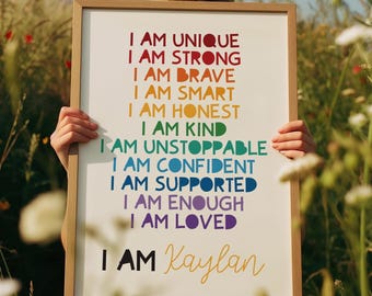 Könnte beinhalten: Ein gerahmter Druck mit den Worten "I AM UNIQUE, I AM STRONG, I AM BRAVE, I AM SMART, I AM HONEST, I AM KIND, I AM UNSTOPPABLE, I AM CONFIDENT, I AM SUPPORTED, I AM ENOUGH, I AM LOVED" in Regenbogenfarben. Der Name "Kaylan" ist kursiv geschrieben.