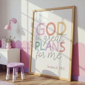 以下が含まれることがあります： カラフルな文字で「GOD has great PLANS for me」と書かれた額入りのプリント。プリントは明るい木製のフレームに入っており、壁に立てかけられています。部屋はピンクと白を基調とした配色です。