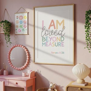 以下が含まれることがあります： パステルカラーで「I AM loved BEYOND MEASURE」と書かれた額入りのプリントがピンク色の壁に掛けられています。小さな花のプリントとピンクの鏡も展示されています。部屋は柔らかくフェミニンなトーンで装飾されています。
