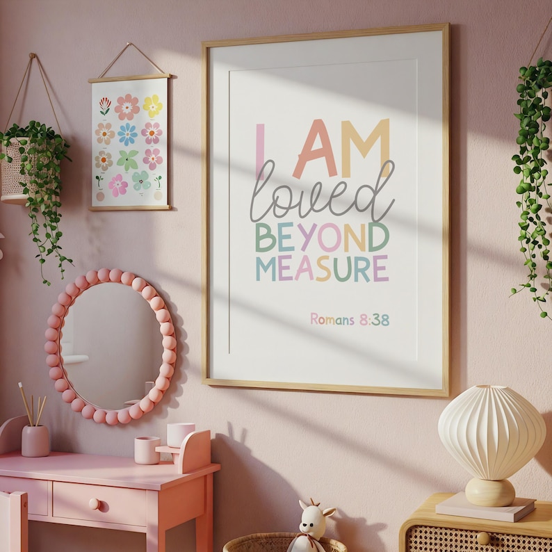 以下が含まれることがあります： パステルカラーで「I AM loved BEYOND MEASURE」と書かれた額入りのプリントがピンク色の壁に掛けられています。小さな花のプリントとピンクの鏡も展示されています。部屋は柔らかくフェミニンなトーンで装飾されています。