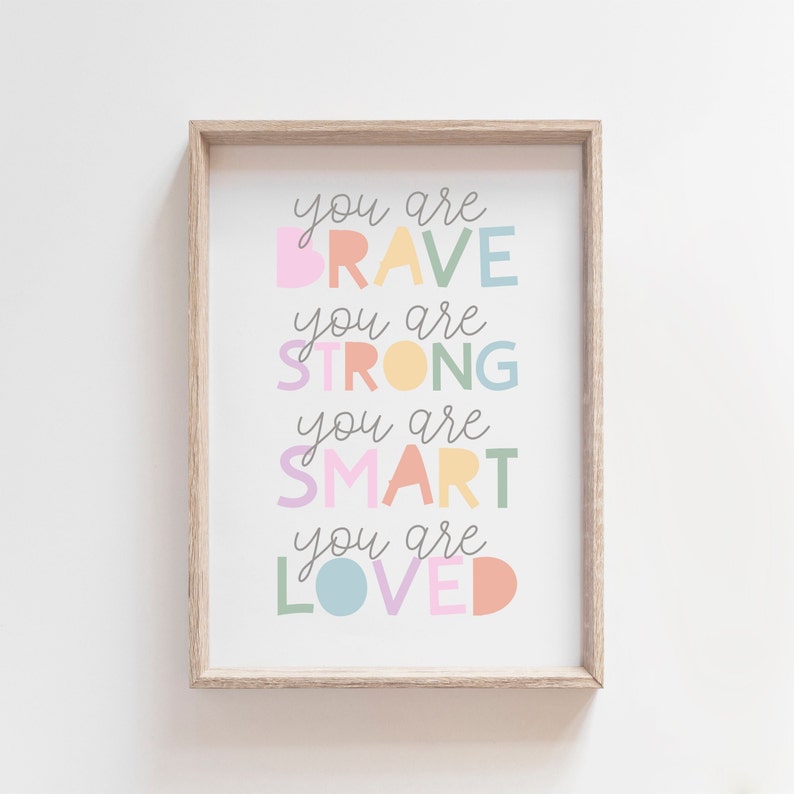 Pu&ograve; includere: Una stampa incorniciata con il testo "you are brave, you are strong, you are smart, you are loved" in lettere colorate su uno sfondo bianco.