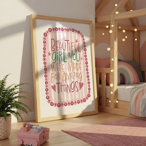 Może przedstawiać: Oprawiony wydruk z napisem "BEAUTIFUL GIRL YOU WERE MADE FOR AMAZING THINGS" w r&oacute;żowo-czerwonym wzorze. Wydruk jest w jasnej drewnianej ramie i opiera się o ścianę w pokoju dziecięcym.