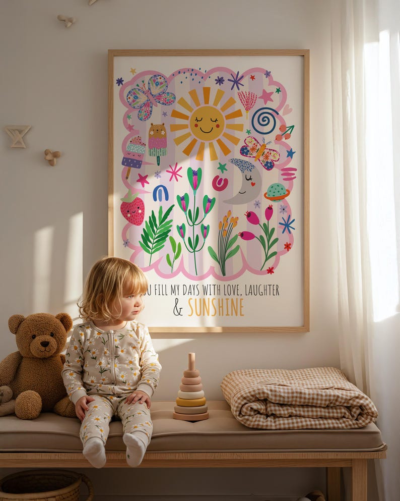 May include: A framed art print with a colorful illustration featuring a smiling sun, butterflies, and flowers. The text reads "YOU FILL MY DAYS WITH LOVE, LAUGHTER & SUNSHINE." A child in a floral onesie sits on a bench with a teddy bear and wooden stacking toy.