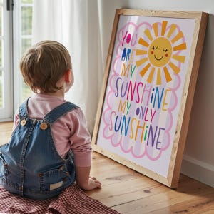 May include: A framed print with the words "You Are My Sunshine, My Only Sunshine" in colorful letters. The artwork features a smiling sun with orange and yellow rays. The frame is made of light-colored wood.