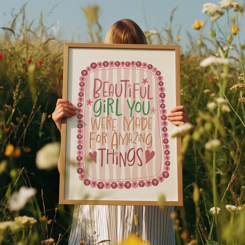 Może przedstawiać: Oprawiony wydruk z napisem "BEAUTIFUL GIRL YOU WERE MADE FOR AMAZING THINGS" w dekoracyjnym wzorze. Nadruk ma jasno r&oacute;żowe i białe paski w tle z r&oacute;żową obw&oacute;dką i akcentami w kształcie serca. Rama jest w jasnobrązowym kolorze.