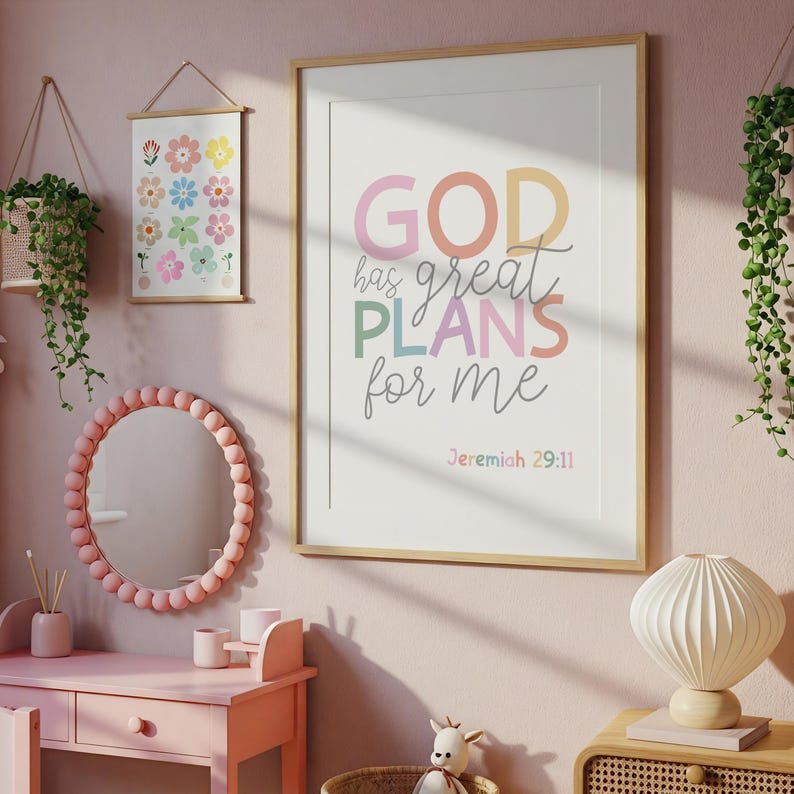 以下が含まれることがあります： パステルカラーで「GOD has great PLANS for me」と書かれた額入りのプリント。小さな花のプリントと、ビーズフレームのピンクの鏡が壁に掛かっています。ピンクの化粧台と装飾的なランプも表示されています。