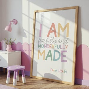 Könnte beinhalten: Ein gerahmter Druck mit den Worten "I AM fearfully and wonderfully made" in Pastellfarben. Der Druck befindet sich in einem hellen Holzrahmen und lehnt an einer Wand. Ein kleiner Hocker und ein Beistelltisch befinden sich im Vordergrund.