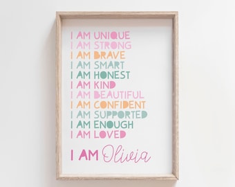 Puede incluir: Una impresión enmarcada con fondo blanco y texto rosa, naranja y turquesa que dice "Soy única, soy fuerte, soy valiente, soy inteligente, soy honesta, soy amable, soy hermosa, soy segura de mí misma, soy apoyada, soy suficiente, soy amada, soy Olivia".