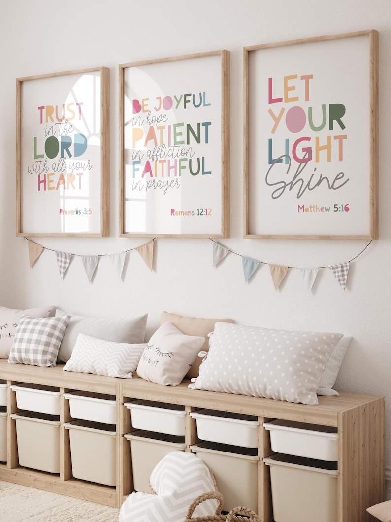 May include: Three framed prints with colorful text and bible verses. The prints are hung on a white wall above a wooden bench with pillows. The text on the prints reads "Trust in the Lord with all your heart", "Be Joyful in hope, Patient in affliction, Faithful in prayer", and "Let your light shine".