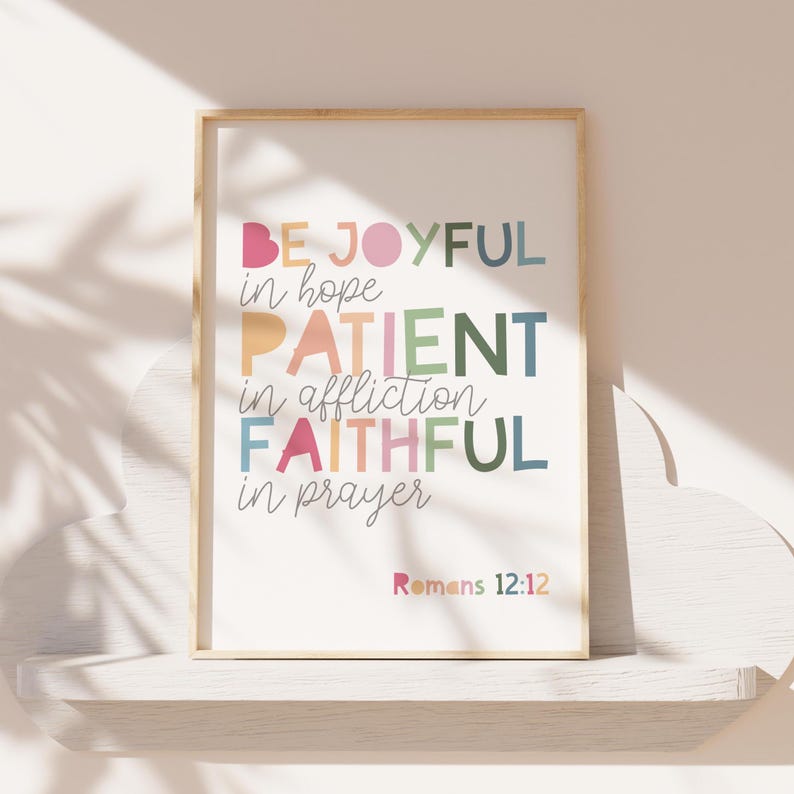 May include: A framed print with a white background and colorful text that reads "Be Joyful in hope, Patient in affliction, Faithful in prayer." The text is in a variety of colors, including pink, orange, yellow, green, blue, and purple. The bottom of the print reads "Romans 12:12".