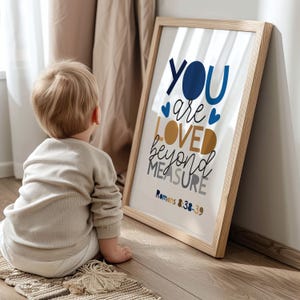 Könnte beinhalten: Ein gerahmter Druck mit den Worten "YOU are LOVED beyond MEASURE" in Blau, Gold und Grau, mit dem Bibelvers Römer 8:38-39. Ein Kind sitzt auf dem Boden und betrachtet den gerahmten Druck. Der Rahmen ist aus hellem Holz.