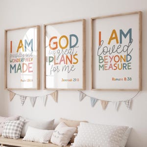 Puede incluir: Tres impresiones artísticas enmarcadas con citas inspiradoras en letras coloridas. Las impresiones están en marcos de madera y cuelgan sobre un banco con almohadas. Las citas incluyen "I AM fearfully and wonderfully MADE", "GOD has great PLANS for me" y "I AM loved BEYOND MEASURE".