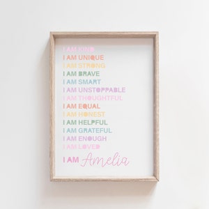 May include: A framed print with the words "I AM" followed by positive affirmations in various pastel colors. The name "Amelia" is written in a cursive font at the bottom. The frame is a light wood color.