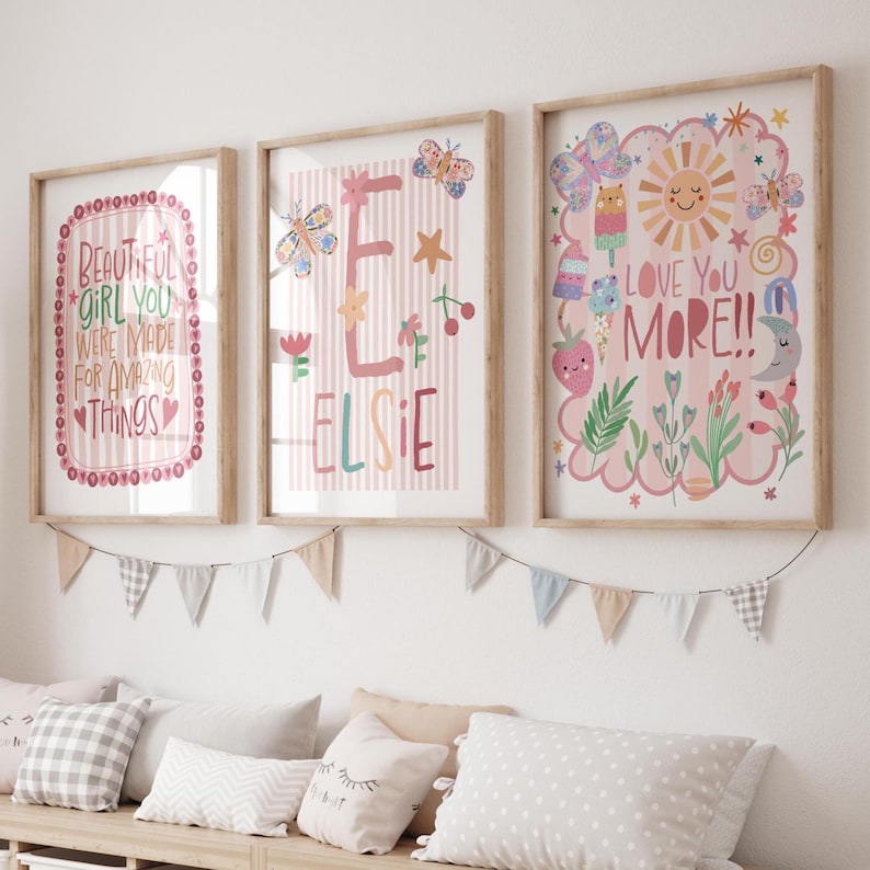 Może przedstawiać: Trzy oprawione wydruki artystyczne z drewnianymi ramami. Wydruki zawierają kolorowe ilustracje i tekst, w tym "Beautiful Girl You Were Made For Amazing Things", imię "Elsie" i "Love You More!!" Poniżej wiszą dekoracyjne proporczyki.