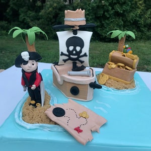 May include: A blue and white pirate ship cake with a skull and crossbones on the sail, a pirate figure, a treasure chest, and a treasure map.