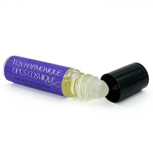 May include: A perfume oil roller bottle with a purple label reading "Yox Harmonique Opus Cosmique". The clear bottle contains a yellow liquid, and the black cap is off. The label also says "Perfume Oil / Huile de Parfum".