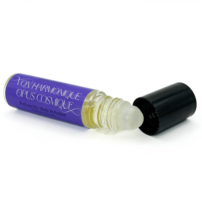 May include: A perfume oil roller bottle with a purple label reading "Yox Harmonique Opus Cosmique". The clear bottle contains a yellow liquid, and the black cap is off. The label also says "Perfume Oil / Huile de Parfum".