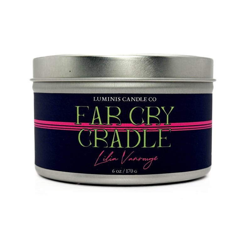 Peut inclure: Une bougie en m&eacute;tal argent&eacute; avec une &eacute;tiquette bleu marine. L'&eacute;tiquette pr&eacute;sente le texte "FAR CRY CRADLE" en vert et rose, avec "Luminis Candle Co" au-dessus et "Lilia Vansrouge" en dessous. La bougie p&egrave;se 170 g.