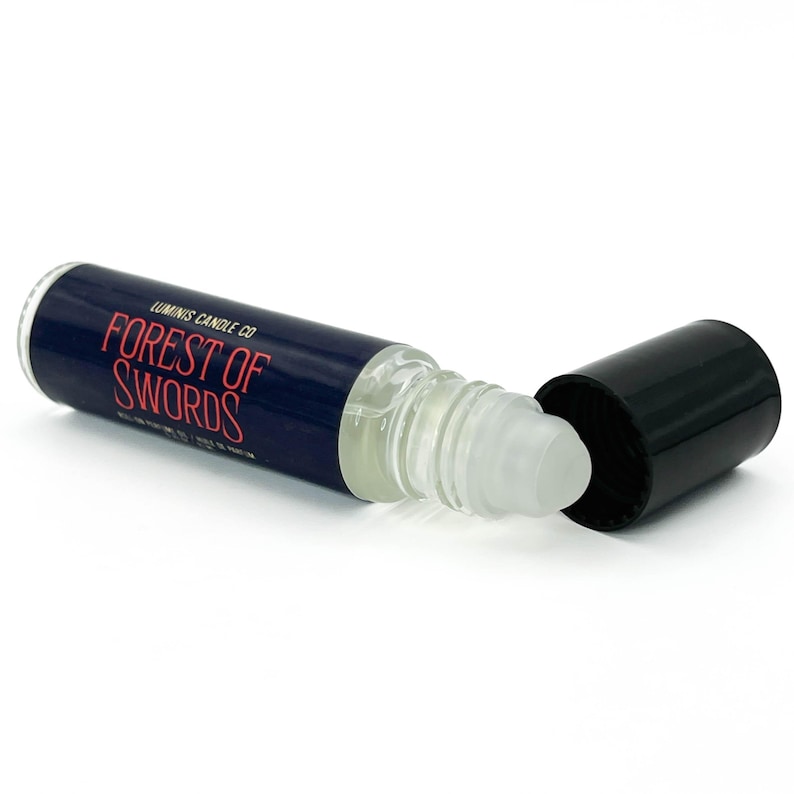 May include: A clear glass roll-on bottle with a dark blue label and the words "FOREST OF SWORDS" in red. The bottle is lying on its side with the black cap removed, revealing the rollerball applicator.