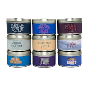 May include: Nine metal tin candles with various labels. The labels feature phrases like "Dread Wolf," "Coffee with the Crows," and "Home Roost." Each candle is 4 oz / 113 g. The candles have a silver lid and a colored label.
