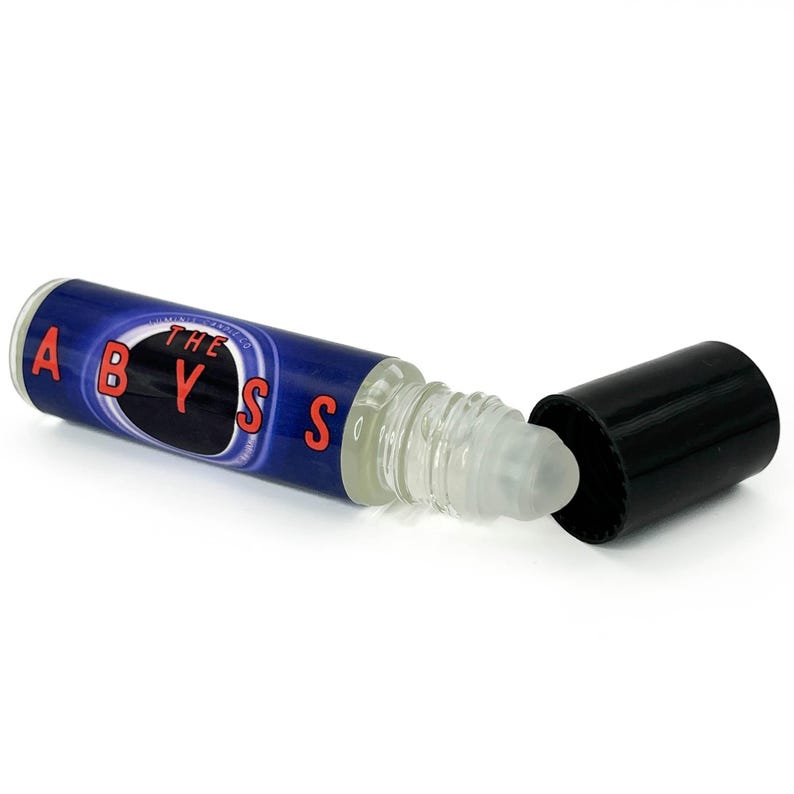May include: A clear glass roll-on bottle with a blue label featuring the word "ABYSS" in red letters. The bottle is lying on its side with the black cap removed, revealing the rollerball applicator.