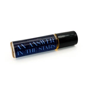 Puede incluir: Un frasco de perfume roll-on con tapa negra y etiqueta azul oscuro. La etiqueta dice "AN ANSWER IN THE STARS" en texto blanco. El frasco contiene un líquido de color dorado.