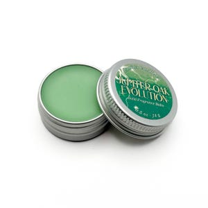 May include: Two small, silver-colored tins of solid fragrance balm. One tin is open, revealing a light green balm. The other tin is partially open, displaying the text "JEPHER-OAK EVOLUTION Solid Fragrance Balm" on a green label. Each tin contains 0.5 oz (14 g).