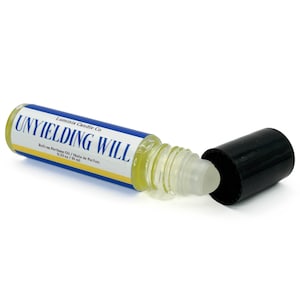 May include: A clear roll-on perfume oil bottle with the text "UNYIELDING WILL" in blue and white. The bottle contains a yellow liquid. The black cap is off, showing the rollerball. The product is from Luminis Candle Co.