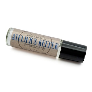 May include: A clear glass roll-on perfume oil bottle with a black cap. The label features the text "Luminis Candle Co" and "ATELIER'S KEEPER" in blue, along with "Roll-on Perfume Oil / Huile de Parfum" and "0.33 oz / 10 ml" in black.