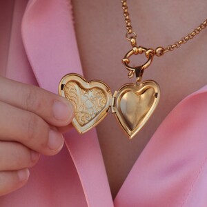 May include: A gold heart-shaped locket necklace with a detailed floral design on the inside of the locket.