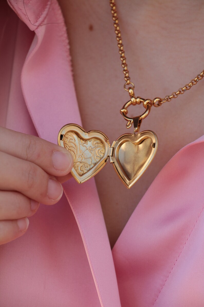May include: A gold heart-shaped locket necklace with a detailed floral design on the inside of the locket.