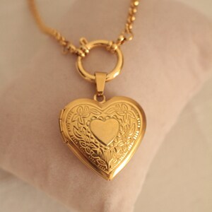 May include: A gold heart-shaped locket necklace with a delicate chain and a floral design. The locket has a small heart-shaped opening in the center.