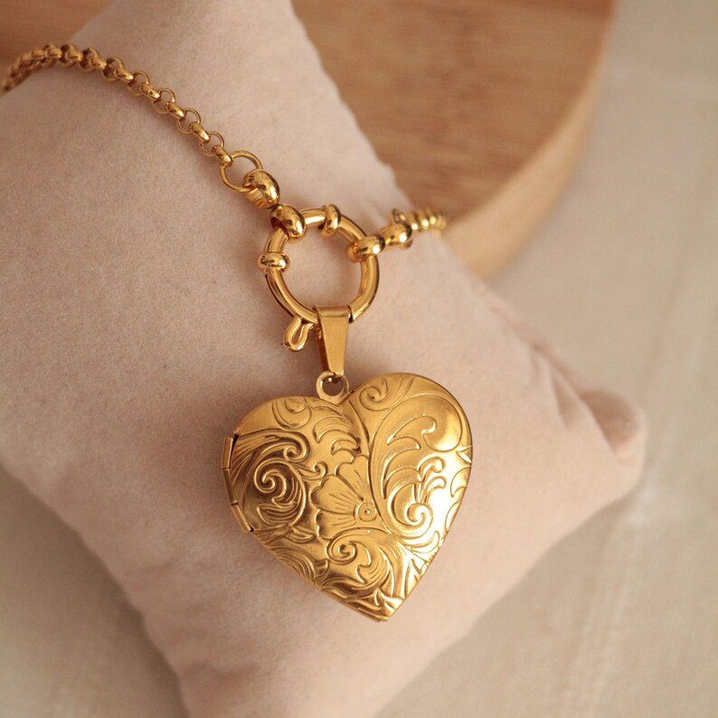 May include: A gold heart-shaped locket necklace with a delicate chain and a detailed floral design. The locket has a clasp closure and is perfect for holding a small photo or message.