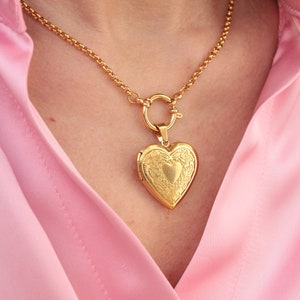 May include: A gold chain necklace with a heart-shaped locket pendant. The locket has an intricate design and is closed.