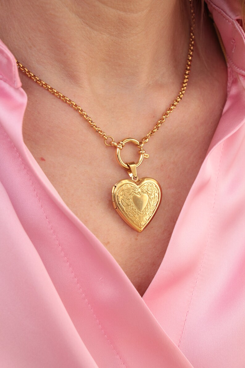 May include: A gold chain necklace with a heart-shaped locket pendant. The locket has an intricate design and is closed.