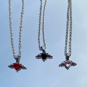 Op de afbeelding: Drie zilveren kettingen met gevederde hart hangers. De harten zijn versierd met rode, zwarte en roze edelstenen.