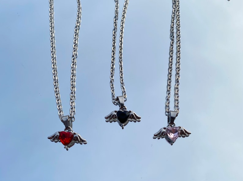 Op de afbeelding: Drie zilveren kettingen met gevederde hart hangers. De harten zijn versierd met rode, zwarte en roze edelstenen.
