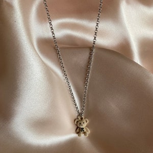 Puede incluir: Un collar de cadena plateada con un pequeño dije de oso de peluche marrón.