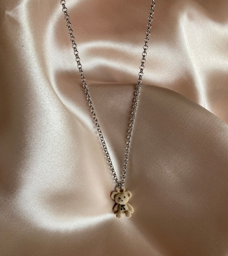 May include: A silver chain necklace with a small brown teddy bear charm.