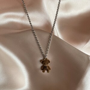 May include: A silver chain necklace with a brown teddy bear charm.