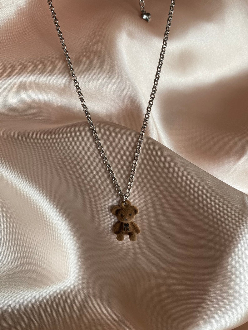 May include: A silver chain necklace with a brown teddy bear charm.