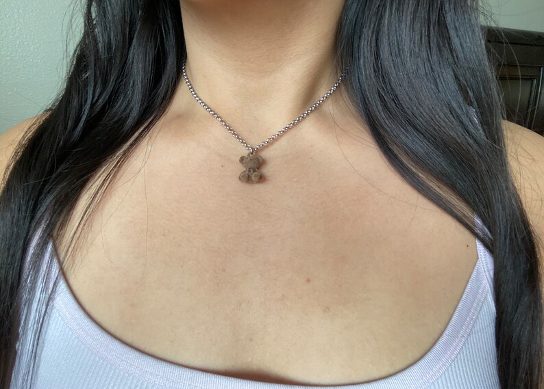 May include: A silver chain necklace with a small brown teddy bear charm.