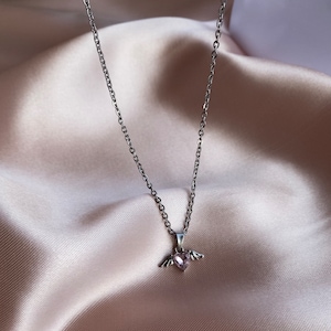 Op de afbeelding: Een zilveren ketting met een klein roze hartje met vleugels.