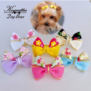 Peut inclure: Plusieurs nœuds pour chiens aux couleurs vives, avec des motifs floraux et dorés. Les nœuds sont roses, jaunes, bleus et violets. L'image présente également un petit chien avec des nœuds dans les cheveux et le texte "Koquettes Dog Bows".