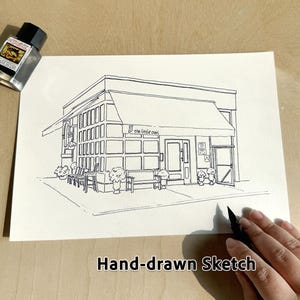 May include: Hand-drawn sketch of a building with the text "the little owl" above the door. The sketch is in black ink on white paper. A bottle of ink is in the upper left corner. The words "Hand-drawn Sketch" are at the bottom.