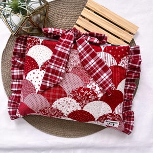 May include: A red and white patchwork pillow with a ruffled edge and a plaid bow. The pillow features a variety of red and white patterned fabrics in a fan-like design. A small tag with the text "Rainstorm J&Y" is visible.
