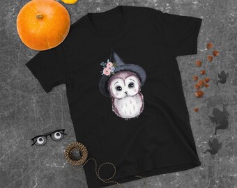 May include: Black t-shirt with a cute cartoon owl wearing a witch hat with pink flowers. The owl has big eyes and a white and gray body.