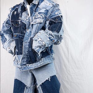 May include: A patchwork denim jacket and matching jeans. The jacket features a mix of light and dark blue denim patches with distressed edges. The jeans have a similar patchwork design. The outfit is a unique take on denim fashion.